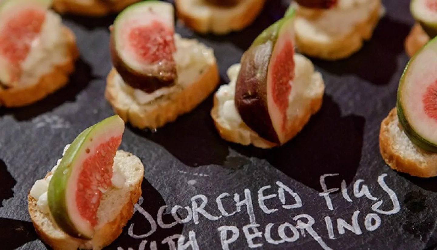 Crostinis topped with pecorino cheese and fresh figs on a black slate board.